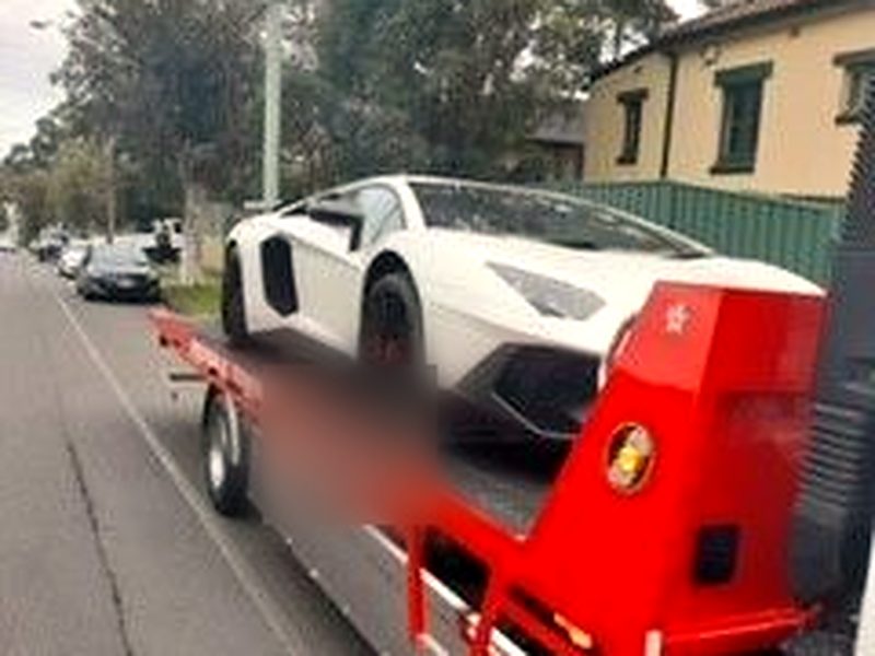 White Lamborghini secured on a red tilt-tray tow truck on a suburban street