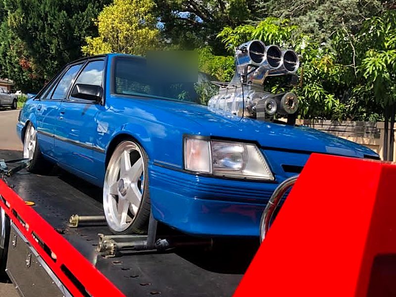 Blue VK Holden Commodore with a supercharger blower, strapped on a red tilt tray