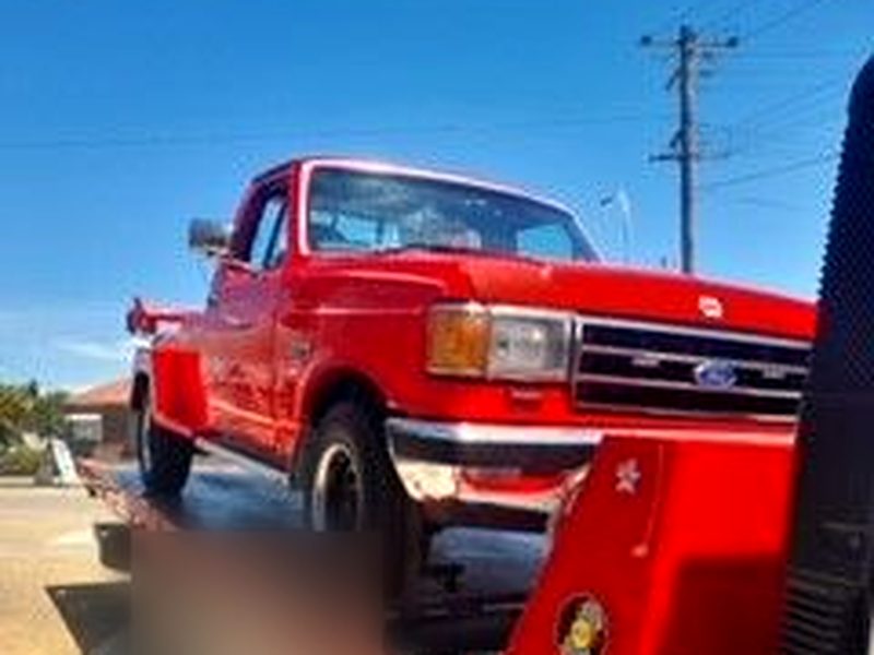 Red classic Ford F-series pickup on a tilt-tray tow truck