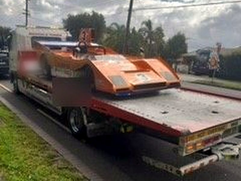 Orange open-wheel race car loaded on a tilt-tray tow truck